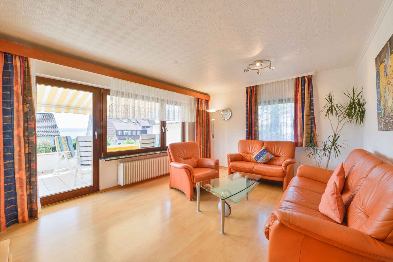 Wohnung 1 - Erdgeschoss Helles Wohnzimmer mit orangefarbenen Sofas, Glas-Tisch und Fenstern zur Terrasse.