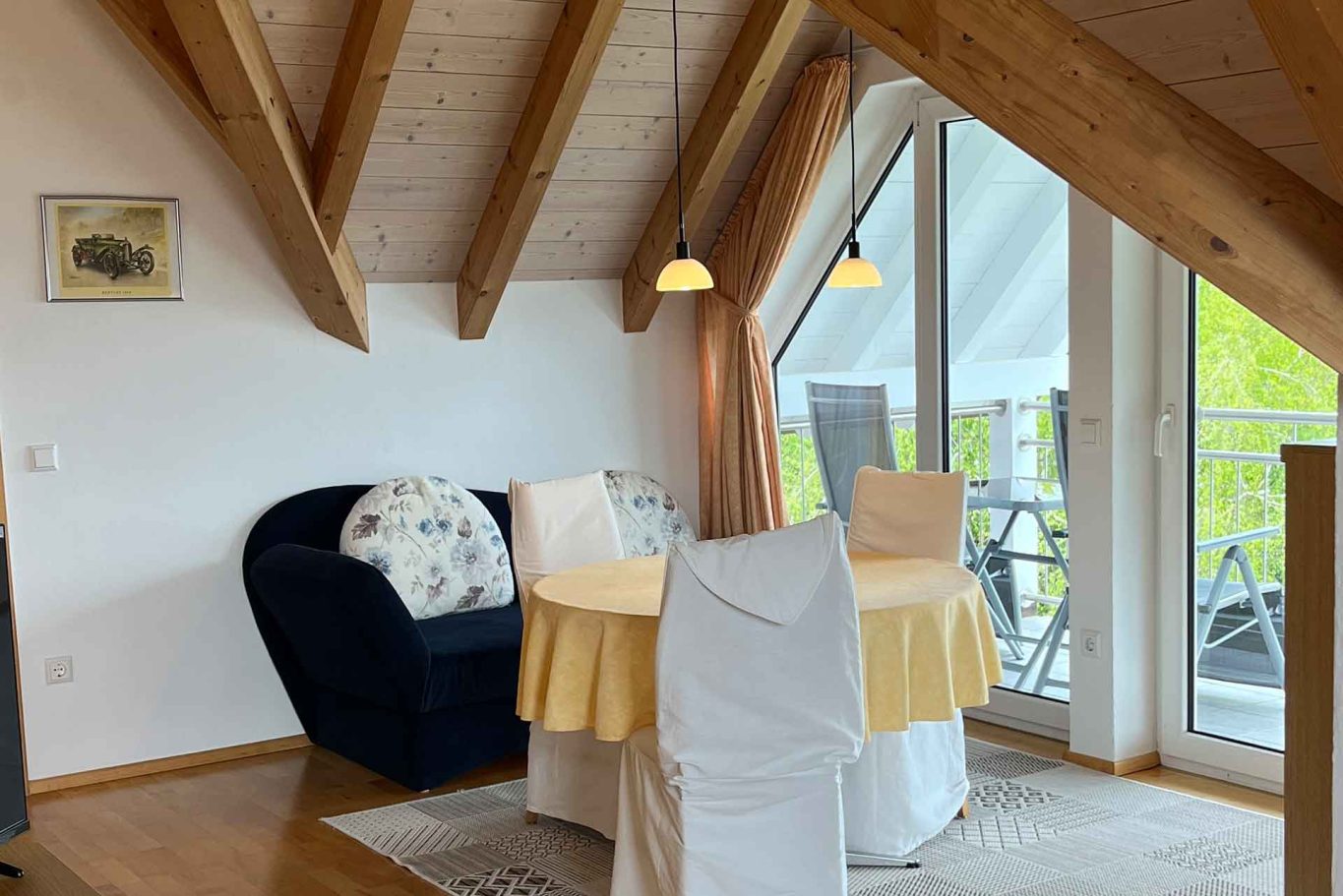 Wohnung 3 - Dachwohnung mit Balkon Heller Wohnbereich mit Sitzungstisch und Sofabereich unter einem Holzgebälk.